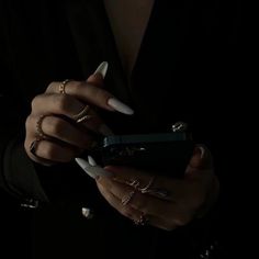 a woman with white nails holding a cell phone in her hand and wearing gold rings