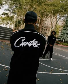 two men standing on a basketball court with trees and buildings in the backgroud