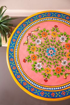 a colorful plate with flowers painted on it sitting next to a potted plant in a room