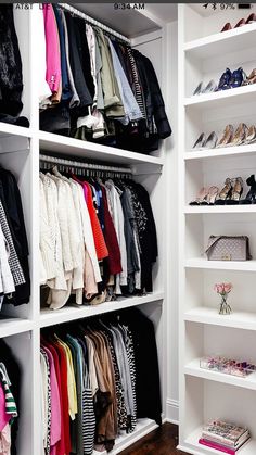 an organized closet with white shelving and lots of clothes on hangers in it