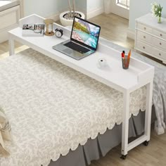 a laptop computer sitting on top of a white desk next to a bed in a room