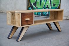 a wooden table sitting on top of a sidewalk next to a graffiti covered wall and door