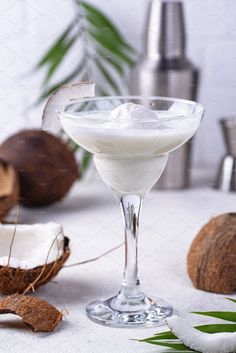 a glass filled with white liquid next to coconuts