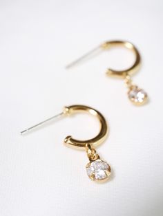 "Modern huggie hoop earrings with a sparkly cubic zirconia gem for a little sway and shimmer. Dangling from secure sterling silver stud hoops for secure and easy wear. MATERIALS [ SILVER ] sterling silver hoop, rhodium silver filled charm, AAAAA cubic zirconia [ GOLD ] 14k gold vermeil hoop, 14k gold filled charm, AAAAA cubic zirconia DIMENSIONS ◊ hoops measure 11mm (7/16\") in diameter and about 1.5mm (1/16\") thick ◊ 21mm (13/16\") length with drop ◊ 4mm (5/32\") gem ◊ More cz jewelry: https:/ Small Hoop Cubic Zirconia Crystal Earrings, Dainty Cubic Zirconia Jewelry With Dangling Charms, Dainty Huggie Jewelry With Prong Setting, Dainty Hoop Jewelry With Prong Setting, Dainty Diamond Dangle Hoop Earrings, Dainty Cubic Zirconia Hoop Jewelry, Dainty Huggie Charms Jewelry, Dainty Huggie Earrings With Charms And Dangle Shape, Dainty Dangle Huggie Earrings With Charms