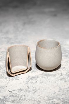 two small white bowls sitting on top of a table next to each other in front of a gray background