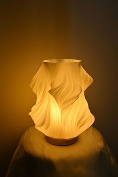 a white vase sitting on top of a table next to a light bulb in the dark