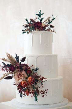 a three tiered white wedding cake with flowers and foliage on the top, sitting on a table