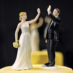 a bride and groom figurine on top of a yellow tableclothed cake