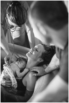 a black and white photo of a woman holding a baby in a bathtub with two other people around her