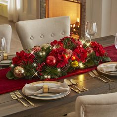 a christmas table setting with red flowers and greenery