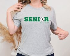 Graduating Class of 2024 Senior Soccer T-Shirt in Gray, Great for a graduation gift! Introducing the ultimate blend of softness, style, and comfort! Our unisex t-shirt is like a cozy hug from your favorite person, but in clothing form. It's made from 100% combed and ring-spun cotton, which means it's as smooth as a baby's bottom and will feel like a dream against your skin. Plus, with a modern fit and a ton of color options, you'll look as good as you feel. Whether you're hitting the gym, lounging at home, or just want to show off your impeccable taste in fashion, this shirt has got you covered. Literally! Taking care of your t-shirt is easier than taking care of a houseplant, but just as important if you want it to thrive: -If your t-shirt is feeling a bit grubby, give it a wash in some c White Crew Neck T-shirt For College Events, School Spirit Crew Neck T-shirt With Custom Print, Custom Print Short Sleeve T-shirt For Graduation, College Crew Neck Shirt With Custom Print, Custom Print Crew Neck Shirt For Graduation, Crew Neck T-shirt For College Events With Fan Apparel, Custom Print Crew Neck T-shirt For College, Casual Custom Print T-shirt For College Events, Casual T-shirt With Custom Print For College Events