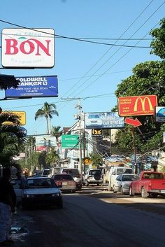 cars are parked on the street in front of stores and billboards that read bon