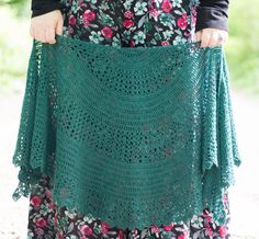 a woman holding up a green crocheted shawl with flowers on the sides