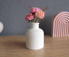 a white vase with pink flowers in it on a table next to a rainbow sculpture