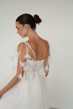 a woman in a white dress with feathers on it's back and shoulder, looking down at the floor