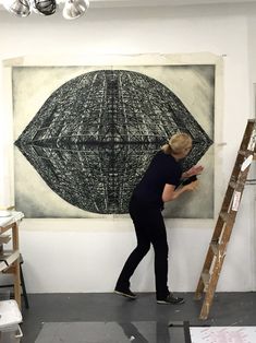 a woman standing in front of a painting on a wall with ladders next to it