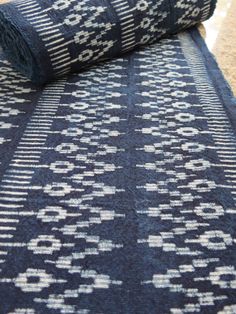 a blue and white rug laying on the ground next to a roll of fabric in front of it