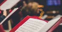 an open book with sheet music on it in front of a group of other people