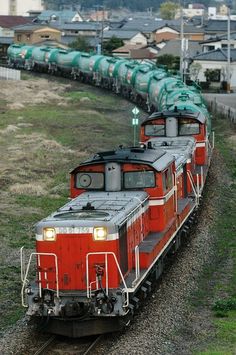 a red train traveling down tracks next to a lush green field with houses in the background