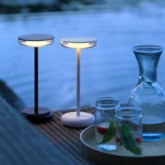 two glass vases sitting next to each other on a wooden table near water and plants