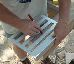 a man is holding a piece of wood and using a pencil to cut it out