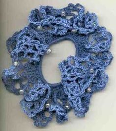 a blue crocheted scarf hanging on the wall with silver beads and pearls around it