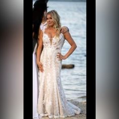 a woman in a wedding dress standing next to another woman on the beach with her hands on her hips