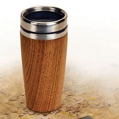 a cell phone is laying next to a wooden cup on the ground with sand around it