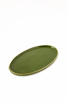 a green oval plate with gold trim on the edge, sitting on a white surface