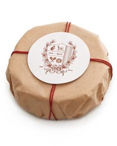 a round gift box wrapped in brown paper with a red ribbon around the top and bottom