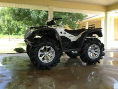 a white and black four - wheeler parked in front of a garage with trees on the side