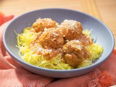 meatballs and spaghetti in a blue bowl on a pink cloth with orange napkins