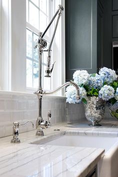 a white sink sitting under a window next to a vase with blue flowers in it