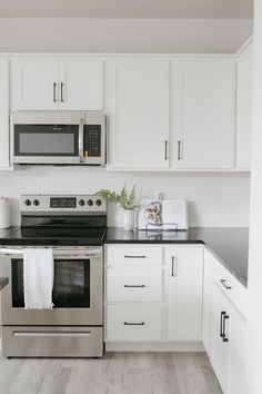 a kitchen with white cabinets and black counter tops, stainless steel stove top oven and microwave