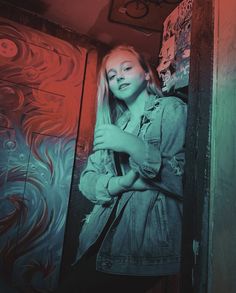 a woman standing in front of a wall with red and blue graffiti painted on it