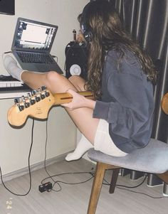 a woman sitting in front of a laptop computer on top of a wooden desk next to a guitar