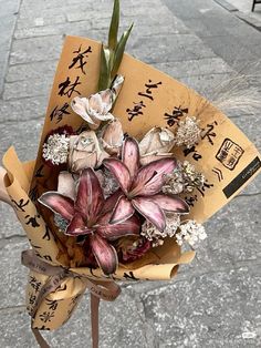 a bouquet of flowers is wrapped in brown paper with writing on the side and attached to a pole