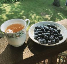 a bowl of blueberries next to a cup of tea on a wooden table outside