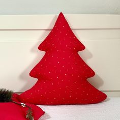 a red christmas tree pillow sitting on top of a bed next to a pink pillow