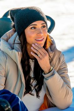 a woman wearing a winter hat and jacket talking on her cell phone while sitting in the snow