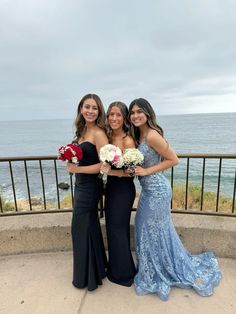 three beautiful women standing next to each other in front of the ocean with their bouquets