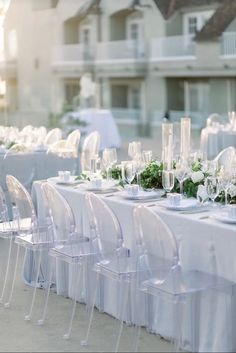 the table is set with clear chairs and place settings