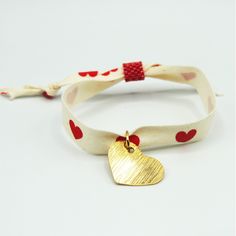 a bracelet with a gold heart charm on it and a red ribbon around the clasp