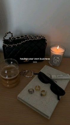 the contents of a woman's purse and jewelry on a table next to a candle