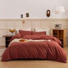 a bed with red sheets and pillows in a white room next to a wooden table