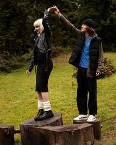 a man and woman standing on top of wooden stumps in front of some trees