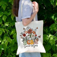 a woman holding a white bag with flowers and butterflies on it that says bbg san diego