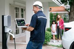 a man using an electric car charger in front of a house with his family