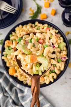 a bowl filled with macaroni salad on top of a blue plate next to a wooden spoon