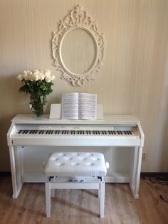 a white piano sitting on top of a hard wood floor next to a vase with flowers